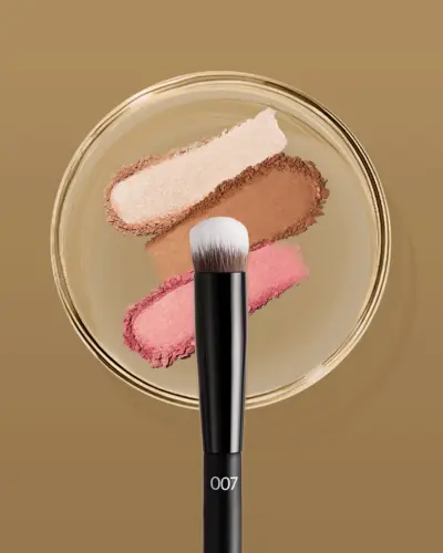 Clean studio product photography, makeup brush displayed over cosmetic powder swatches